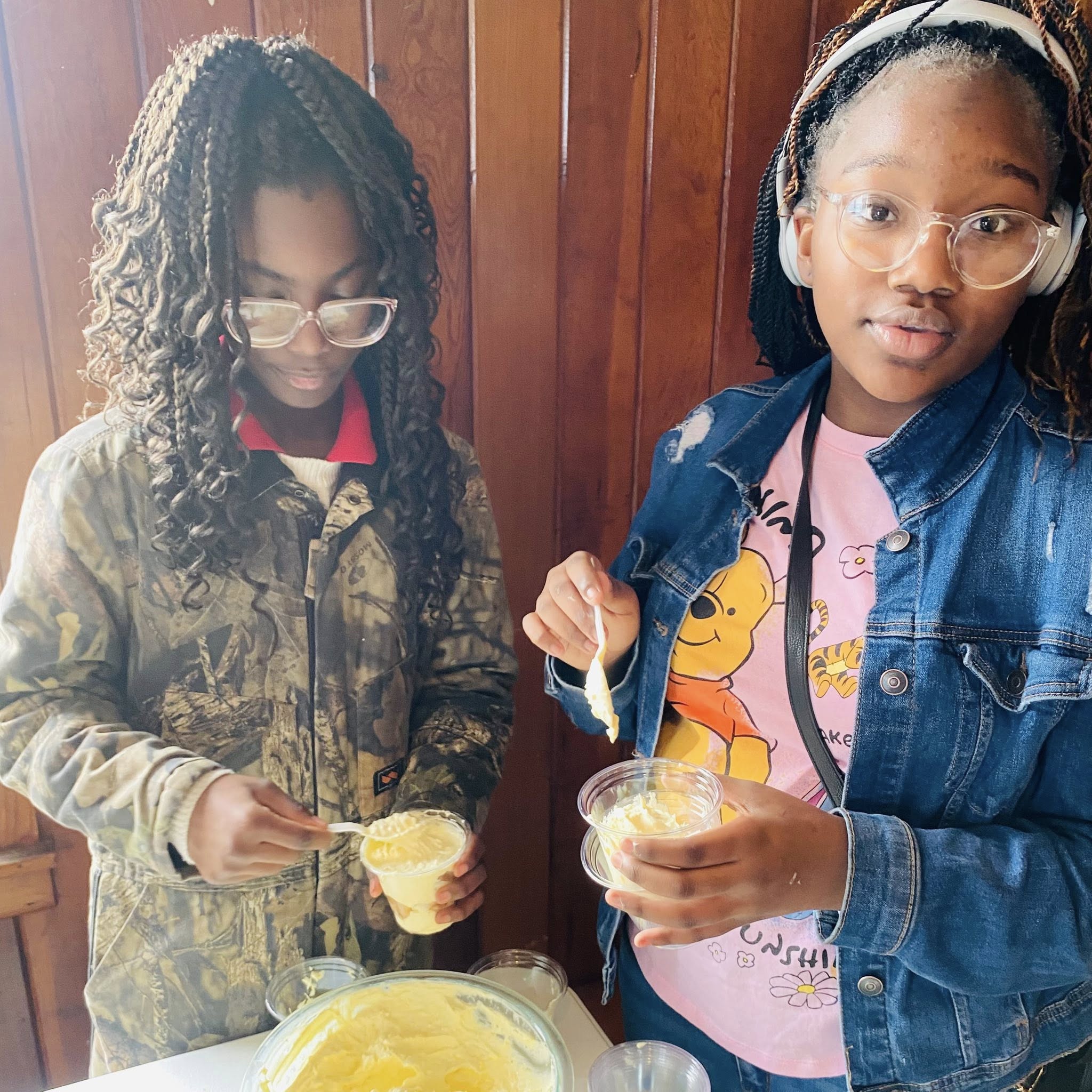 Two girls holding cups with a yellow substance in them.